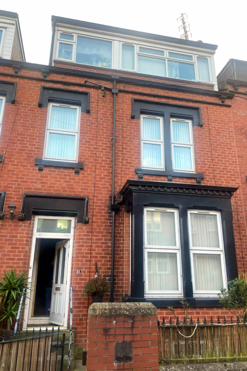 The outside view of a brick terraced house with three windows and a door.