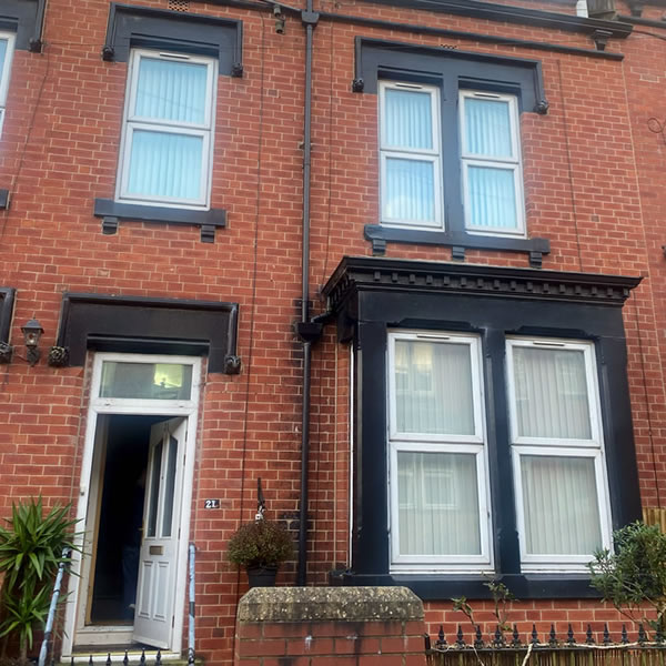 The outside view of a brick terraced house with three windows and a door.