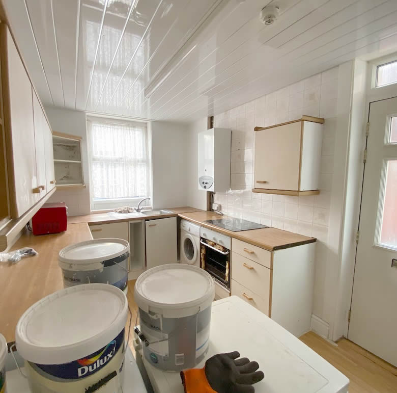 An empty kitchen in the process of being redecorated in the background, pots of paint in the foreground